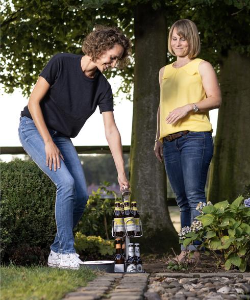 A woman pulls out the bottle scaffolding of a BIERSAFE built into a garden. Another woman watches as she does so.