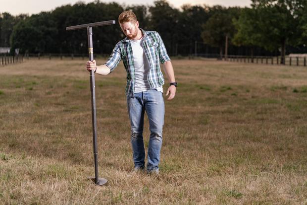 A man drills a hole for the BIERSAFE in a garden with a hand drill